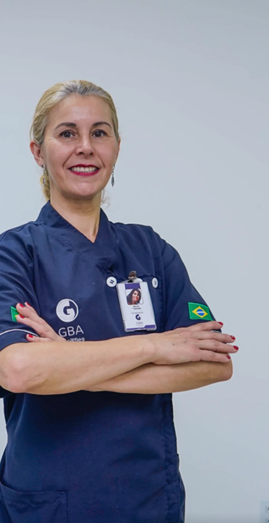 Colaboradora GBA de uniforme, braços cruzados e sorrindo